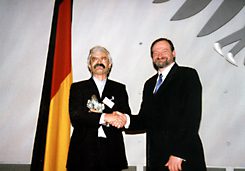 Zwei Herren stehen auf der Bühne im alten Plenarsaal des Bundestages Bonn und schütteln für die Kameras die Hände.